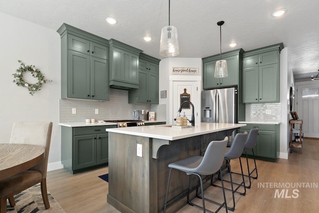 kitchen with a center island with sink, sink, hanging light fixtures, light hardwood / wood-style floors, and stainless steel fridge with ice dispenser