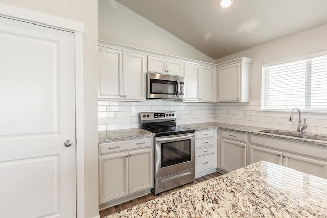kitchen featuring vaulted ceiling, tasteful backsplash, appliances with stainless steel finishes, and a sink