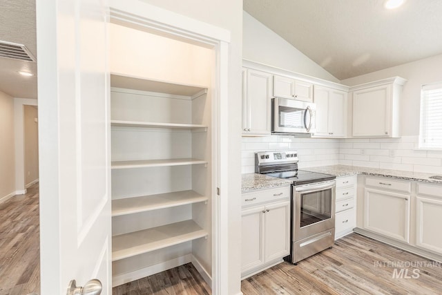kitchen featuring visible vents, stainless steel appliances, white cabinets, light wood finished floors, and vaulted ceiling