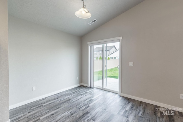 spare room featuring visible vents, a textured ceiling, wood finished floors, baseboards, and lofted ceiling
