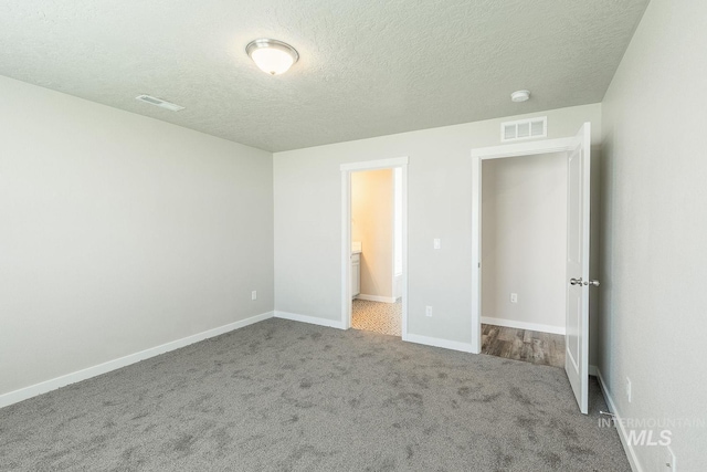 unfurnished bedroom with a textured ceiling, carpet, visible vents, and baseboards