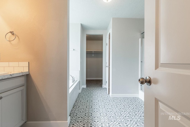 full bathroom with baseboards, a spacious closet, vanity, and a washtub