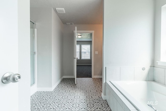 bathroom featuring a garden tub, baseboards, a textured ceiling, and visible vents