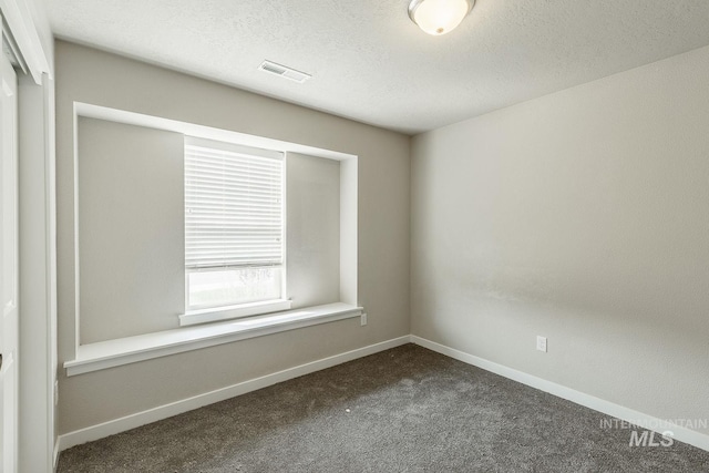 unfurnished room featuring visible vents, baseboards, a textured ceiling, and dark carpet
