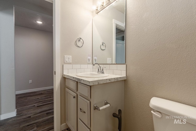 bathroom with baseboards, toilet, wood finished floors, a textured wall, and vanity