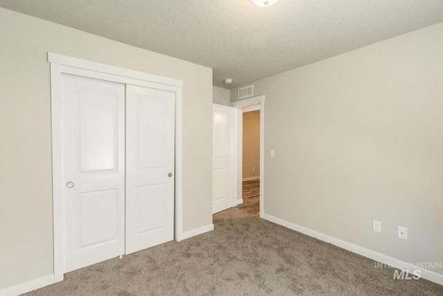 unfurnished bedroom with visible vents, a textured ceiling, a closet, carpet, and baseboards