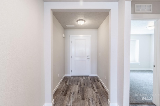 hallway featuring visible vents, a textured ceiling, and baseboards