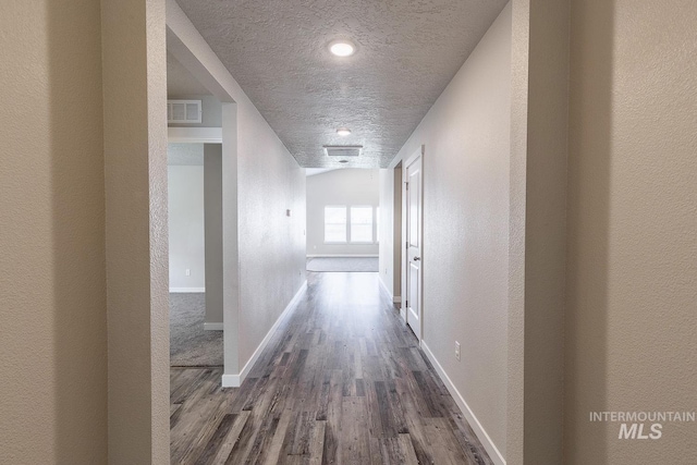 hall with dark wood-style floors, visible vents, a textured ceiling, and baseboards