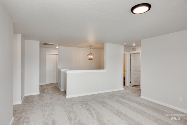 empty room featuring a chandelier, light colored carpet, and a textured ceiling