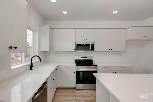 kitchen with sink, backsplash, light wood-type flooring, white cabinetry, and stainless steel appliances