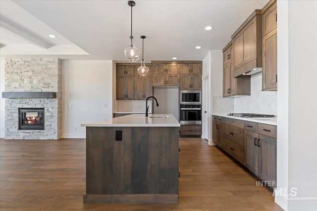 kitchen featuring appliances with stainless steel finishes, pendant lighting, a center island with sink, a fireplace, and dark hardwood / wood-style floors