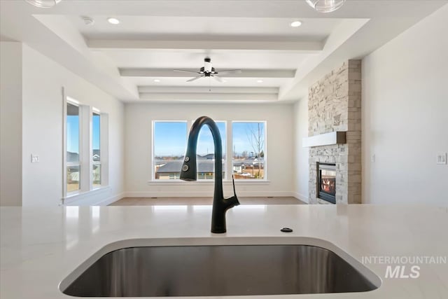 kitchen featuring a tray ceiling, a stone fireplace, a wealth of natural light, and sink