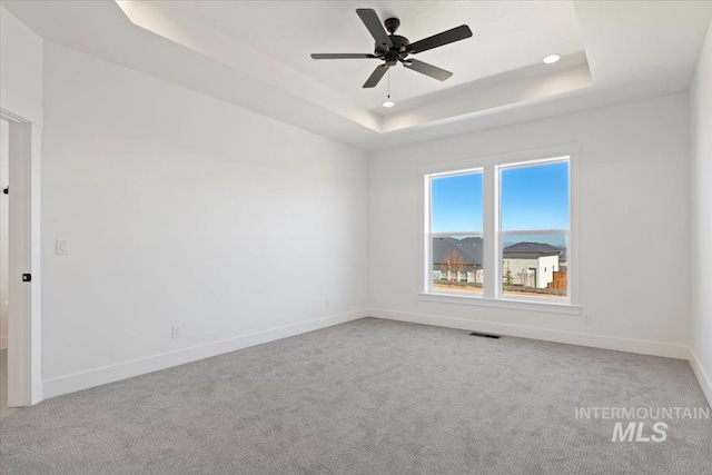 unfurnished room with light colored carpet, a raised ceiling, and ceiling fan