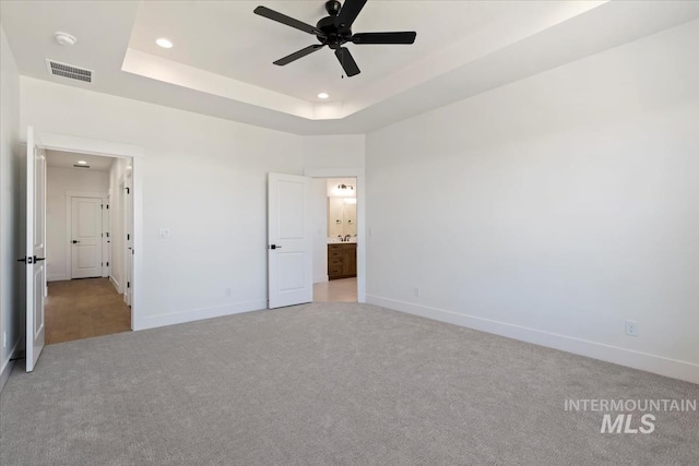 unfurnished bedroom featuring light carpet, a tray ceiling, ceiling fan, and ensuite bathroom