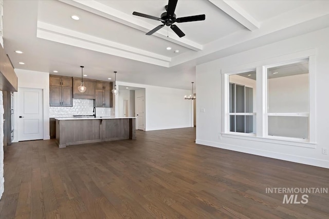 unfurnished living room featuring beamed ceiling, ceiling fan with notable chandelier, dark hardwood / wood-style floors, and sink