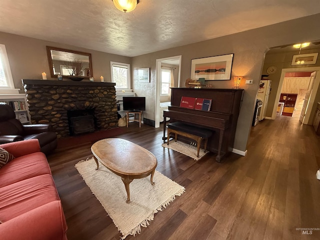 living area with a stone fireplace, a textured ceiling, baseboards, and wood finished floors