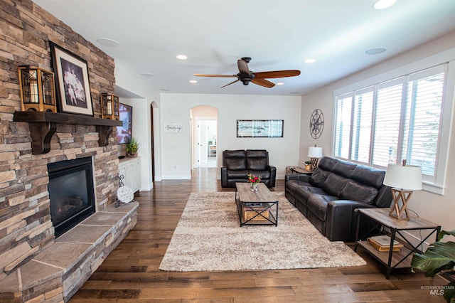 living room featuring arched walkways, dark wood finished floors, a stone fireplace, and recessed lighting