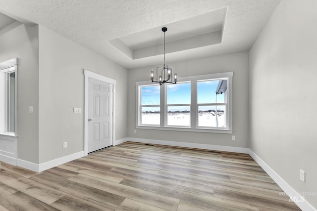 unfurnished dining area featuring light wood-type flooring, a textured ceiling, an inviting chandelier, and a raised ceiling