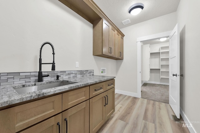 kitchen with light stone countertops, light hardwood / wood-style floors, sink, backsplash, and a textured ceiling