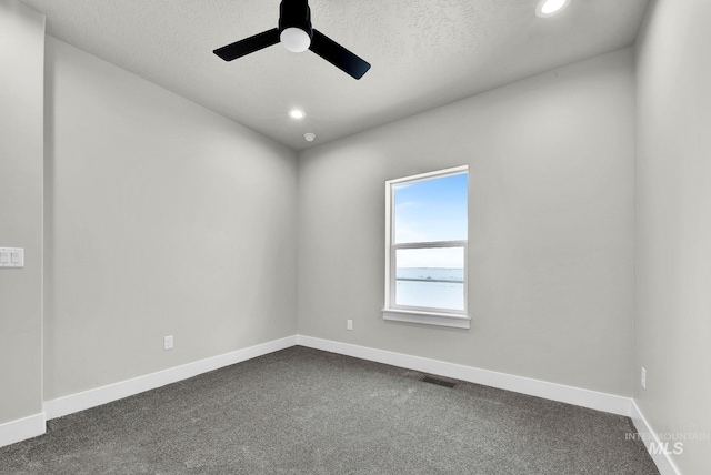 spare room featuring a textured ceiling, dark carpet, and ceiling fan