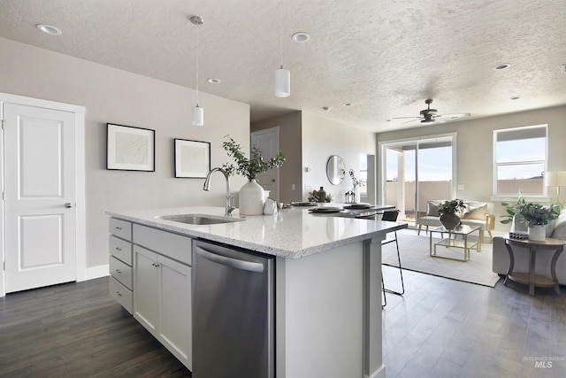 kitchen featuring light stone counters, dark wood-style flooring, stainless steel dishwasher, a sink, and an island with sink