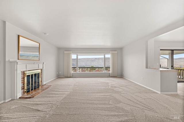 unfurnished living room with a fireplace, plenty of natural light, light colored carpet, and a mountain view