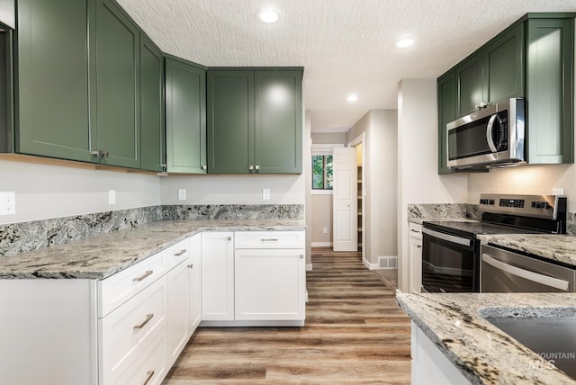 kitchen featuring light hardwood / wood-style flooring, stainless steel appliances, green cabinets, light stone countertops, and white cabinets