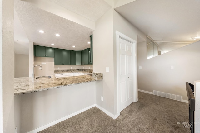 kitchen featuring kitchen peninsula, dark carpet, sink, light stone counters, and green cabinetry