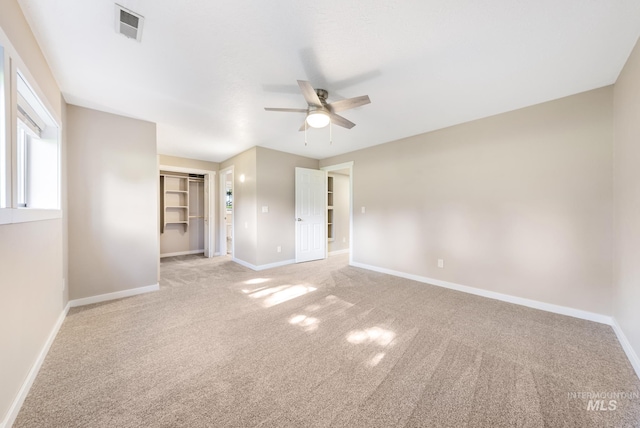 unfurnished bedroom featuring a spacious closet, light colored carpet, a closet, and ceiling fan