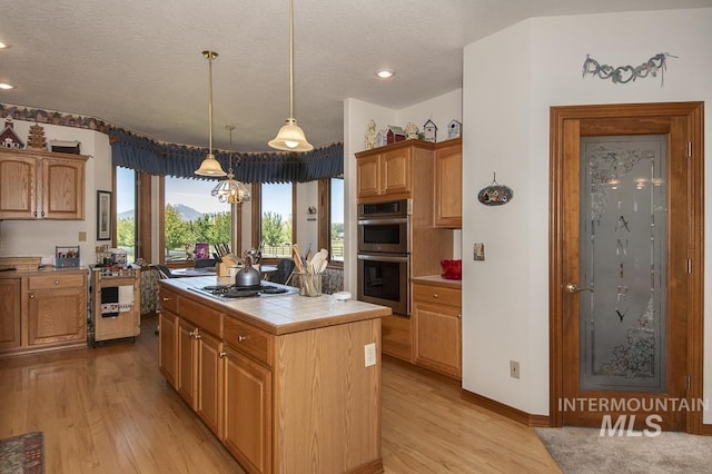 2555 E Quail Run Rd, Emmett, ID 83617 - kitchen with stainless steel appliances, tile countertops, light wood finished floors, a textured ceiling, and a kitchen island