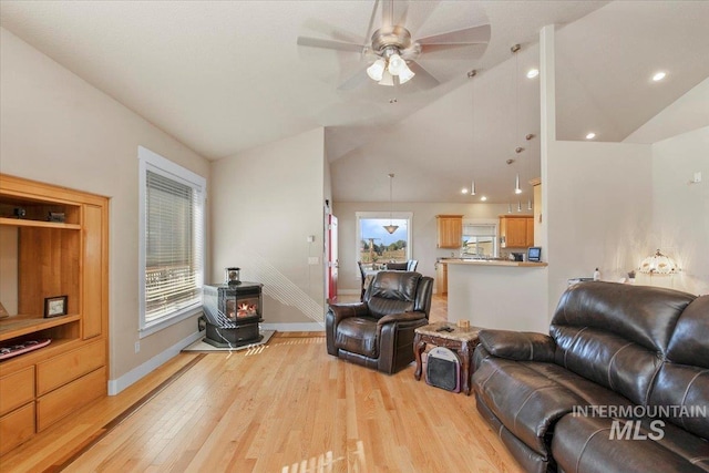 living area with light wood finished floors, baseboards, ceiling fan, a wood stove, and vaulted ceiling