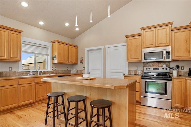 kitchen with a center island, a breakfast bar area, stainless steel appliances, light countertops, and a sink