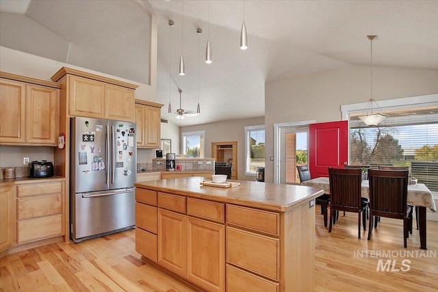 kitchen featuring light brown cabinets, light wood-style flooring, freestanding refrigerator, a center island, and decorative light fixtures