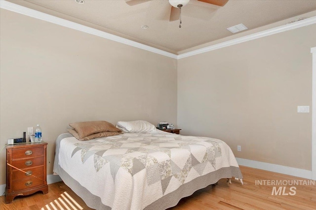 bedroom with visible vents, crown molding, baseboards, and wood finished floors