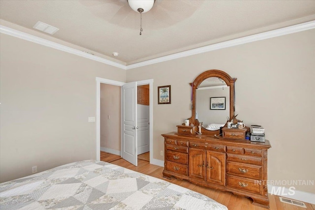 bedroom featuring light wood-style floors, baseboards, visible vents, and crown molding