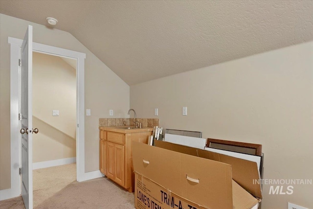 bathroom featuring lofted ceiling, a sink, a textured ceiling, and baseboards