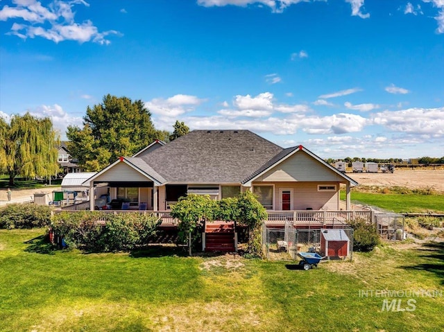 rear view of property featuring roof with shingles, a lawn, and a wooden deck