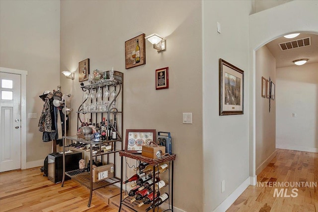 hallway with arched walkways, baseboards, visible vents, and light wood-style floors