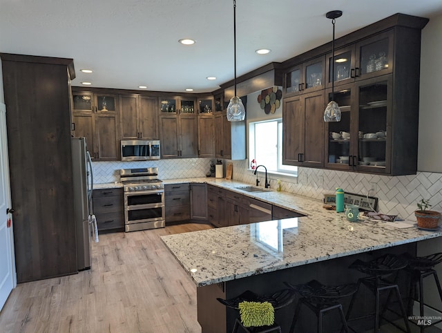 kitchen with sink, light stone counters, decorative light fixtures, kitchen peninsula, and stainless steel appliances