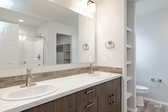 full bathroom featuring double vanity, toilet, a sink, a shower stall, and backsplash