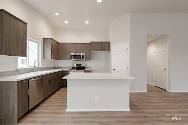 kitchen with appliances with stainless steel finishes, light countertops, a sink, and a center island