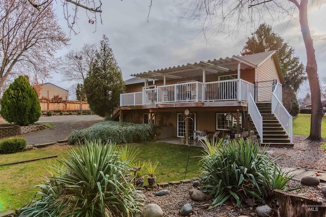 rear view of property featuring a pergola, a wooden deck, and a lawn