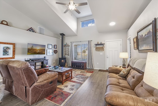 living room with ceiling fan, a wood stove, dark hardwood / wood-style flooring, and a towering ceiling