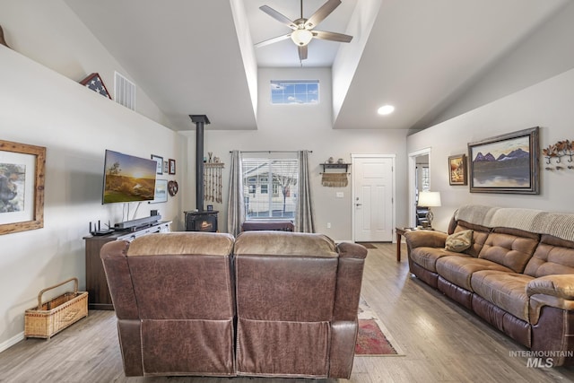 living room featuring ceiling fan, high vaulted ceiling, light wood-type flooring, and a wood stove