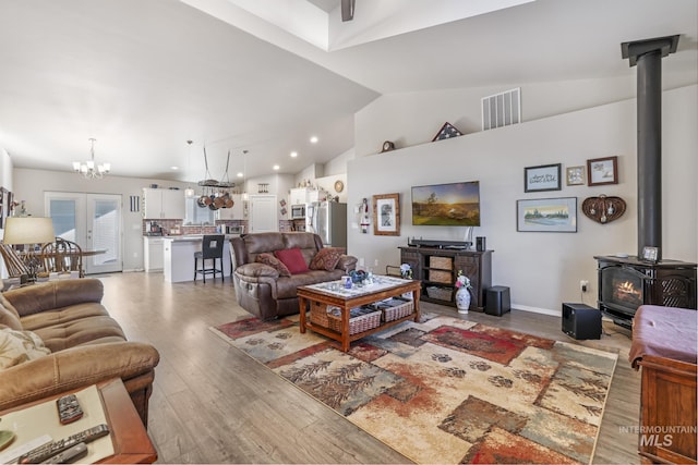 living room with french doors, high vaulted ceiling, hardwood / wood-style floors, and a wood stove