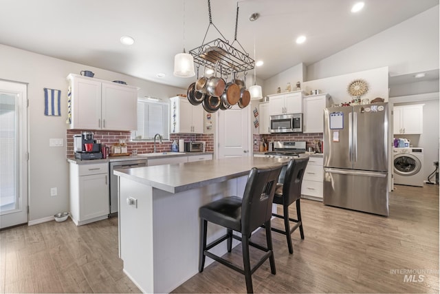 kitchen featuring white cabinetry, a center island, stainless steel appliances, and washer / dryer