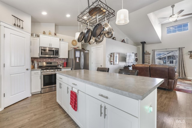 kitchen featuring a kitchen island, appliances with stainless steel finishes, white cabinetry, hanging light fixtures, and light wood-type flooring
