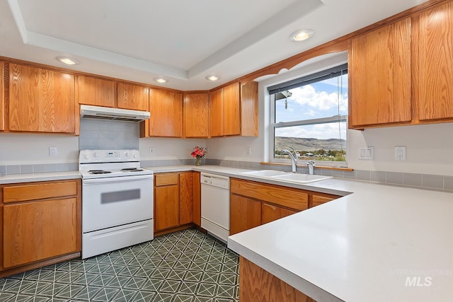 kitchen with a raised ceiling, dark tile patterned flooring, a mountain view, sink, and white appliances