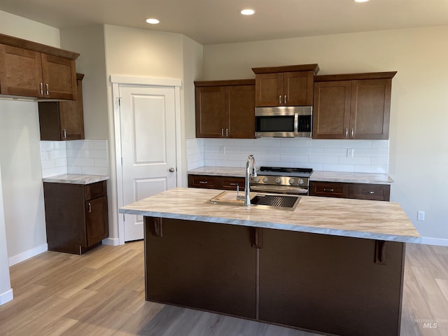 kitchen with appliances with stainless steel finishes, light countertops, a sink, and light wood-style flooring