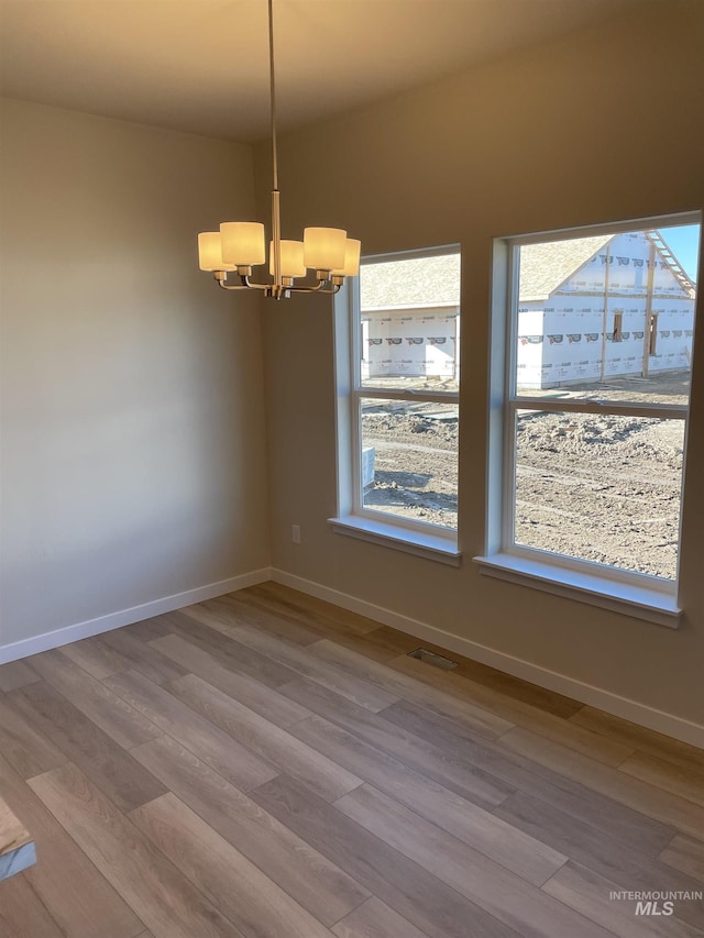 empty room with baseboards, wood finished floors, visible vents, and a notable chandelier